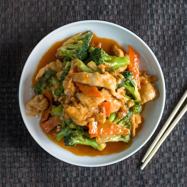 Dragon Dynasty Take Out's chicken and broccoli with carrots in a savory sauce, served with chopsticks.