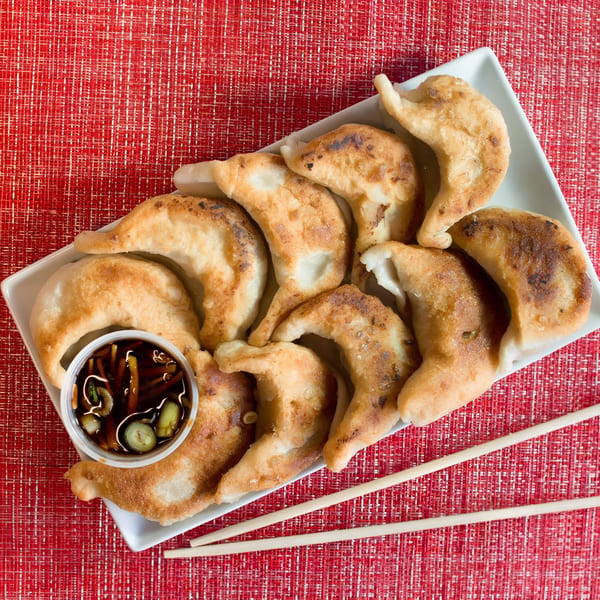 A white rectangular plate of Dragon Dynasty Take Out fried dumplings with dipping sauce and chopsticks.