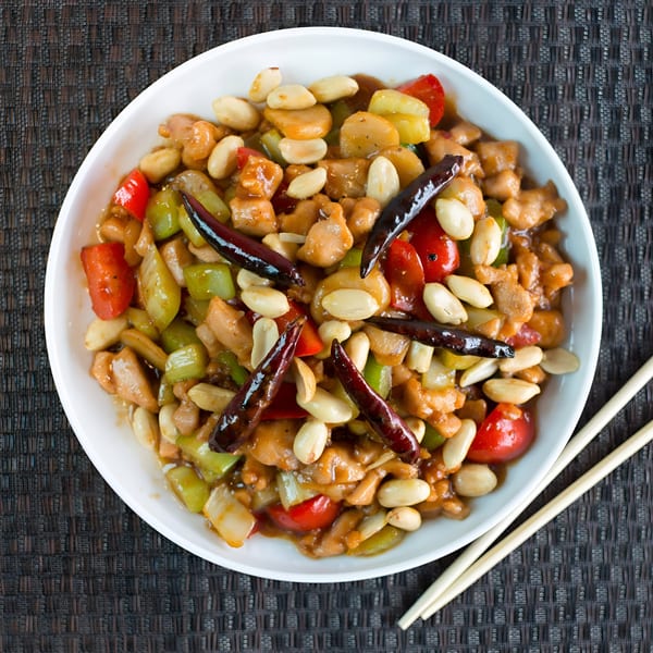 Kung Pao chicken with peanuts, red and green peppers, and dried chilies in a white bowl.
